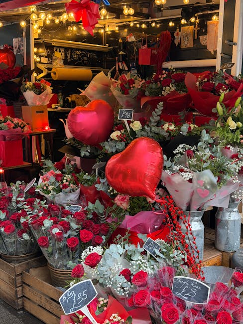 A vibrant display of fresh floral arrangements featuring red roses, white flowers, and eucalyptus greenery, styled in various wrapping papers and ribbons, with some bouquets presented in glass vases. 
